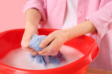 Çamaşırları leğende köpükle yıkayan kadın ve pembe arka planda su, yakın plan.