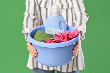 Elinde temiz çamaşırları ve yeşil arka planda bir şişe deterjanı olan bir kadın.