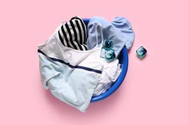 Temiz çamaşır leğeni ve pembe arka planda deterjan kapsülleri.