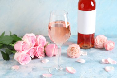 Açık mavi arka planda güzel güllerle dolu bir şişe pembe şarap.