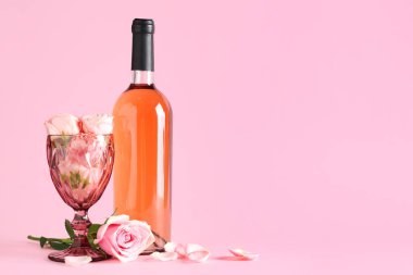 Bir şişe pembe şarap ve arka planda güzel güller olan cam.