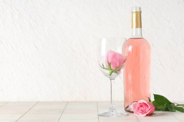 Bir şişe pembe şarap, cam ve beyaz fayans üzerinde güzel güller.