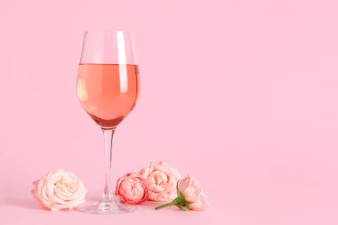 Bir bardak pembe şarap ve arka planda güzel güller.