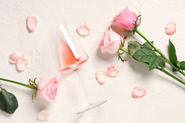 Beyaz arka planda güzel güller ve taç yaprakları olan bir bardak pembe şarap.