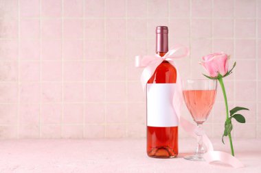 Şişe ve bir bardak pembe şarap, masasında güzel bir gül.