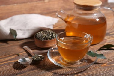 Cam bardak ve çaydanlık, ahşap zemin üzerinde kurumuş yapraklar olan sıcak yeşil çay.