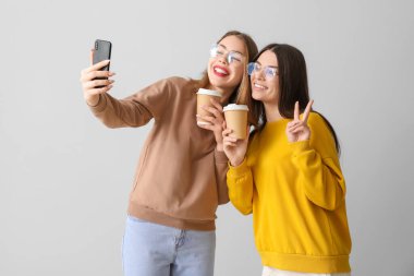 Kahve fincanları olan bayan arkadaşlar arka planda selfie çekiyorlar.