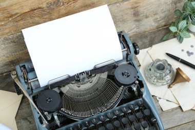 Kahverengi ahşap arka planda klasik daktilo, mürekkep hokkası, çarşaf ve ev bitkisi