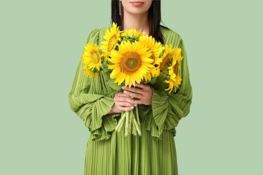 Young woman with beautiful sunflowers on green background