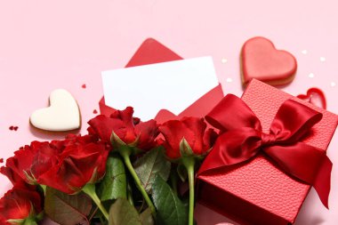 İçinde boş tebrik kartı, kalpler, hediye kutusu ve pembe arka planda bir buket gül olan bir zarf. Sevgililer Günü kutlaması