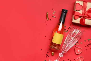İçinde şampanya, cam, hediye kutusu ve kırmızı arka planda mumlar olan kompozisyon. Sevgililer Günü kutlaması