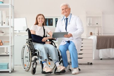 Kırık kollu tekerlekli sandalyedeki genç kadın hastanede doktoru ziyaret ediyor.