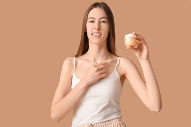 Güzel genç bir kadın kahverengi arka plana kozmetik ürünler uyguluyor.