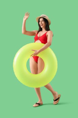 Yeşil arka planda şişirilebilir yüzüklü mayo ve şapka giyen genç ve güzel bir kadın.