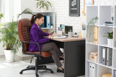 Ofisteki koltukta evrak işi yapan cep telefonlu kadın ofis çalışanı.