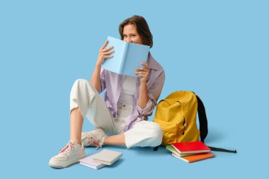 Sırt çantalı güzel bir kız öğrenci ve mavi arka planda oturan kitaplar.