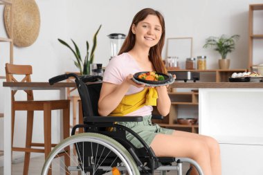Evde kızarmış sebzelerle tekerlekli sandalyede oturan genç bir kadın.