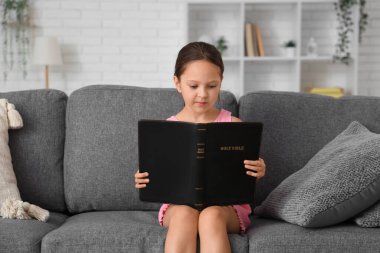 Evdeki kanepede İncil okuyan tatlı küçük kız.