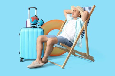 Küreleri ve bavulu olan erkek turist mavi arka planda, iskemlede oturuyor.