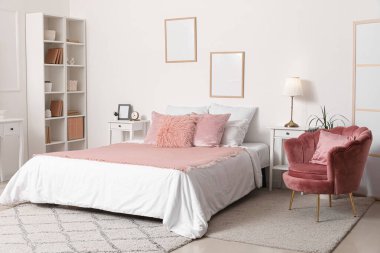 Rahat yatağı, yumuşak koltuğu ve beyaz duvarında resim çerçeveleri olan şık bir yatak odası.