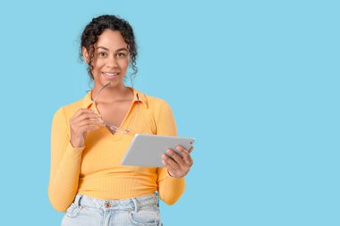 Mavi arka planda tablet bilgisayarı olan genç bir Afro-Amerikan soru cevap mühendisi.