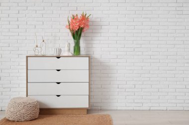 Gladiolus çiçekli vazo, Moai heykeli ve odasındaki beyaz tuğla duvarın yanındaki klozette mumlar.