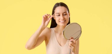 Sarı arka planda pamuk tomurcuklu ve aynalı genç kadın.