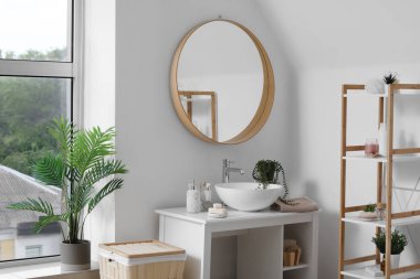 Lavabosu, banyo aksesuarları, aynası ve raf ünitesi olan hafif bir banyo.