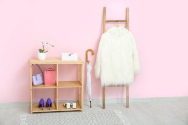 Salondaki pembe duvarın yanında paltosu olan raf, şemsiye ve merdiven.