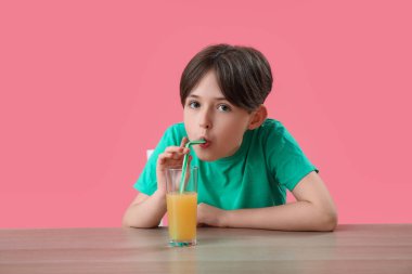 Küçük çocuk pembe arka planda portakal suyu içiyor.