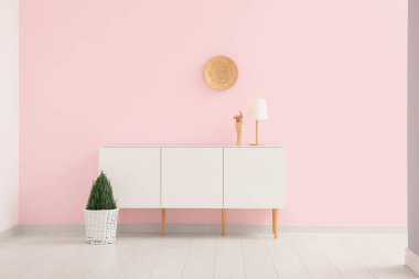 Odadaki pembe duvarda çiçek ve tabak asılı modern çekmeceler.