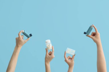 Astım spreyli kadın elleri ve mavi arka planda haplar.