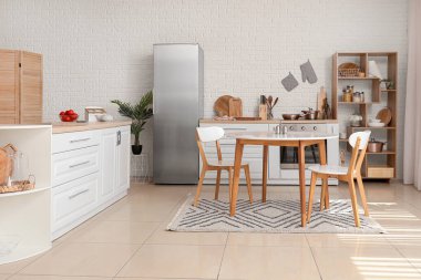 Mutfağın içinde beyaz tezgahlar, buzdolabı ve yemek masası var.