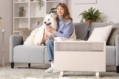 Samoyed köpeği ve ekoseli genç bir kadın evdeki radyatörün yanında ısınıyor.