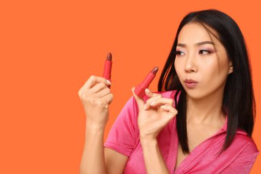 Güzel Asyalı kadın turuncu arka planda ruj seçiyor.