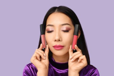 Leylak arkaplanda farklı rujları olan güzel bir Asyalı kadın.