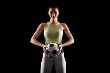 Sporty young woman with soccer ball on black background