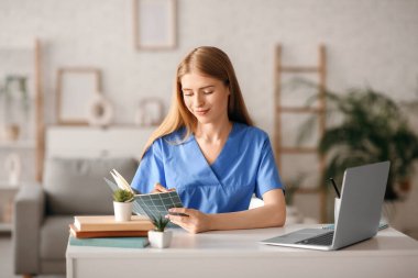 Evde dizüstü bilgisayar ve defterle çalışan kadın stajyer.