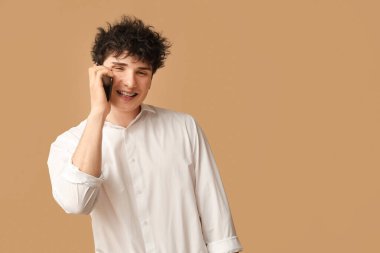 Yakışıklı genç işadamı kahverengi arka planda cep telefonuyla konuşuyor.