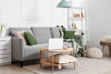 Modern interior of living room with grey sofa and laptop on table
