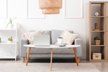 Stylish interior of living room with sofa and modern laptop on table