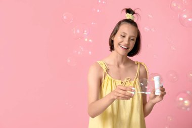 Pembe arka planda sabun köpükleri olan genç bir kız.