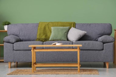 Yeşil duvarın yanında şık gri kanepe ve ahşap sehpa.