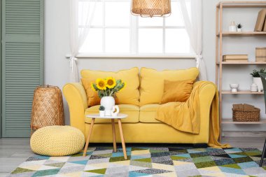 Oturma odasının içinde sarı kanepe ve vazoda ayçiçekleri var.