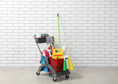 Beyaz tuğla duvarın yanında temizlik malzemeleri ve uyarı levhası var.