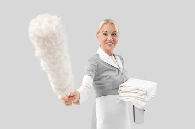 Gri arka planda pp-toz bezi ve temiz havlu yığınıyla orta yaşlı oda hizmetçisi.