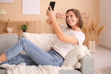 Evdeki kanepede uzanmış selfie çeken güzel bir genç kadın.