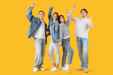 Sarı arka planda kot elbiseli bir grup mutlu genç.