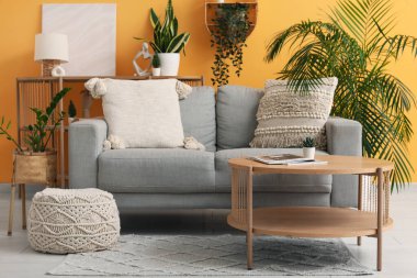 Modern oturma odasının içinde masa ve çiçekli gri bir kanepe.