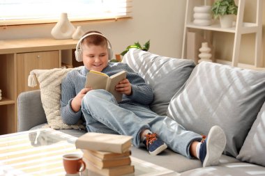 Kulaklıklı küçük çocuk evde kitap okuyor.